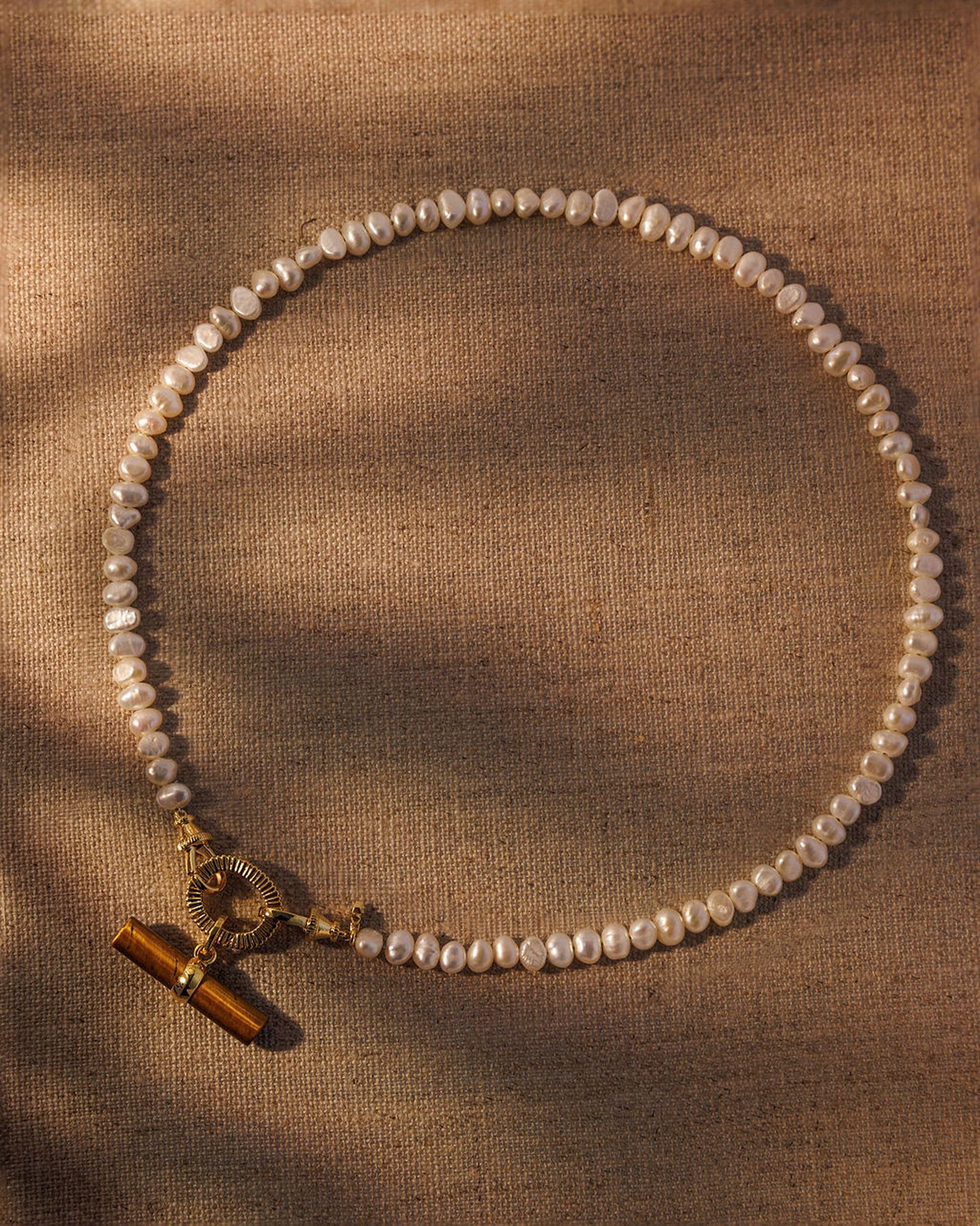 Pearl necklace styled with brown tiger’s eye pendant detail