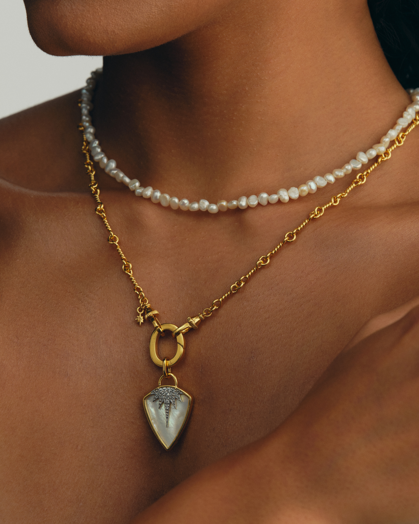 Jumana shield pendant in gold with mother of pearl and crystals on Arabella gold chain with signature oval ring clasp stacked with Aura pearl necklace