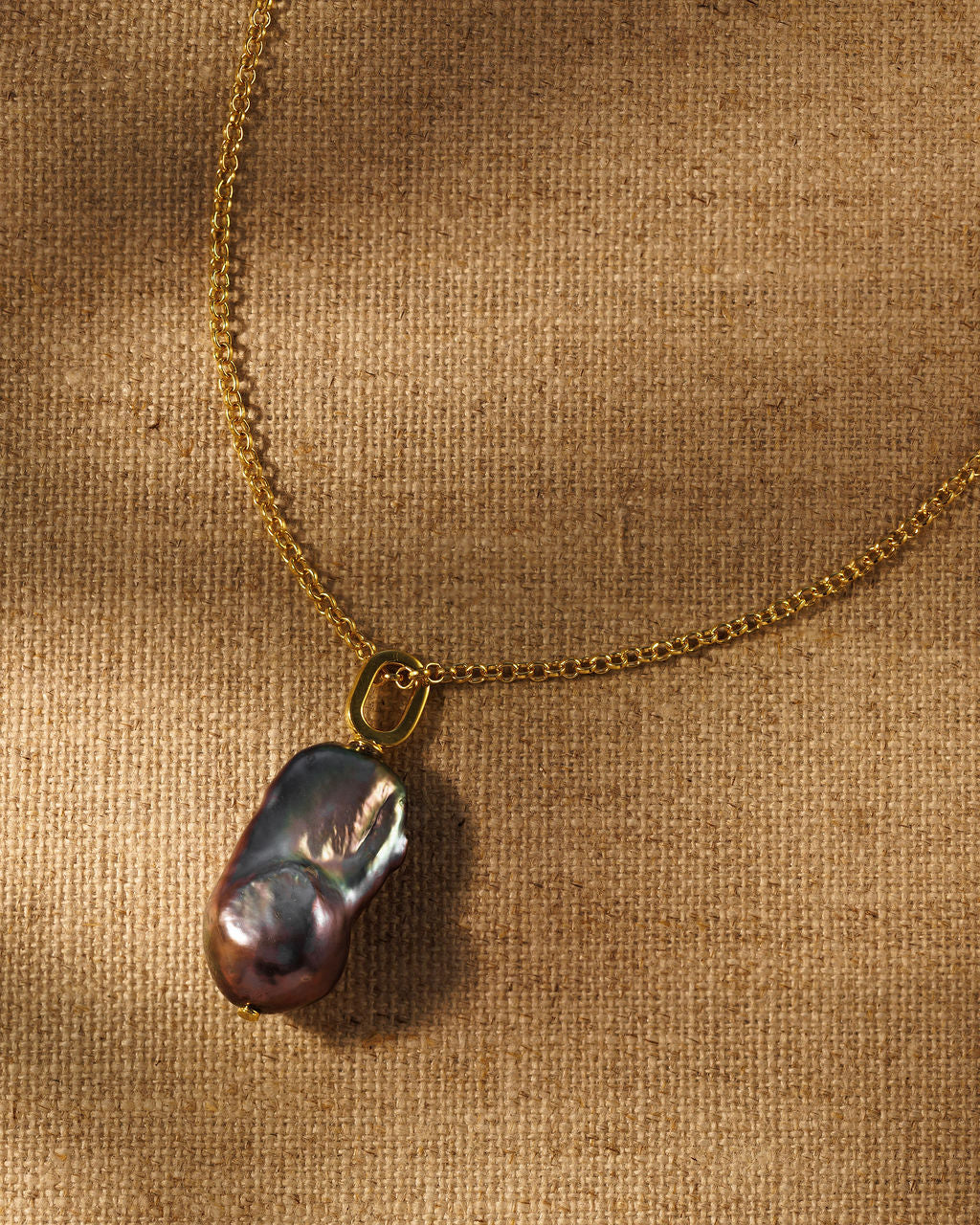 A gold chain necklace with a black baroque pearl pendant