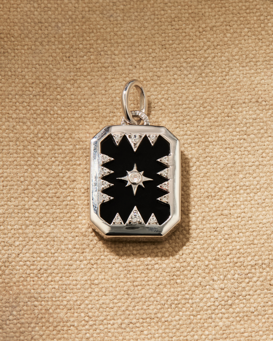 A silver pendant with black onyx and a star design inlay, displayed against a textured background.