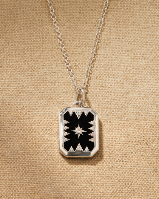 A silver necklace set featuring a rectangular pendant with a black onyx and a star pattern, attached to a fine chain.