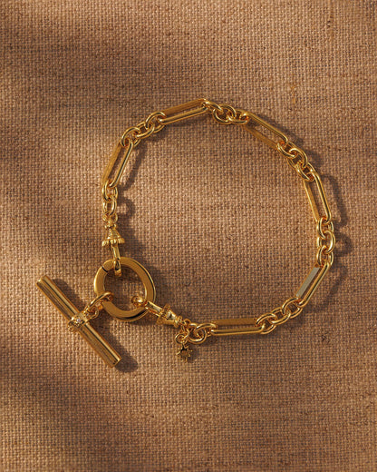 Gold paperclip chain bracelet with T-bar pendant attached to oval clasp