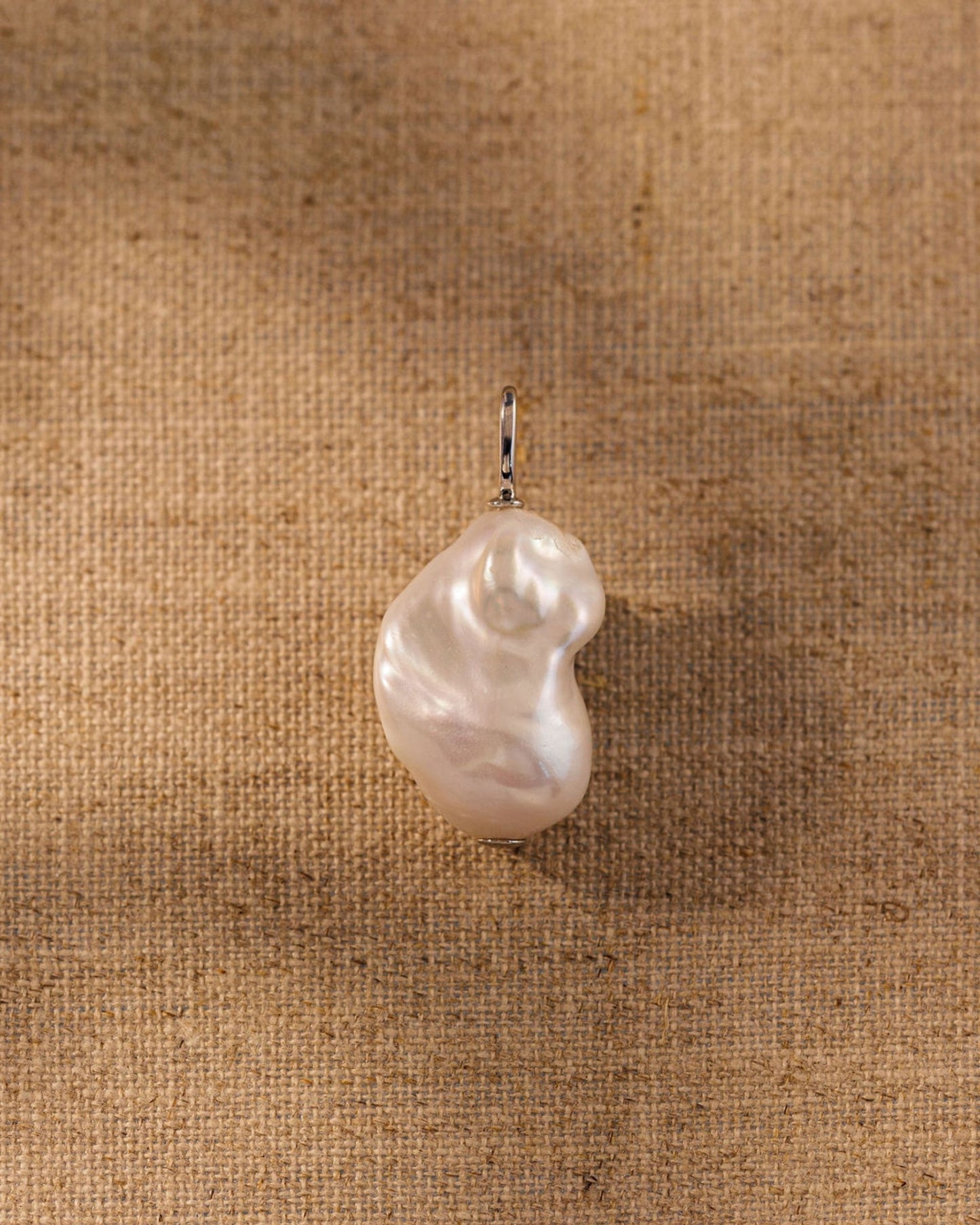 Baroque freshwater pearl pendant charm with sterling silver bail on textured background