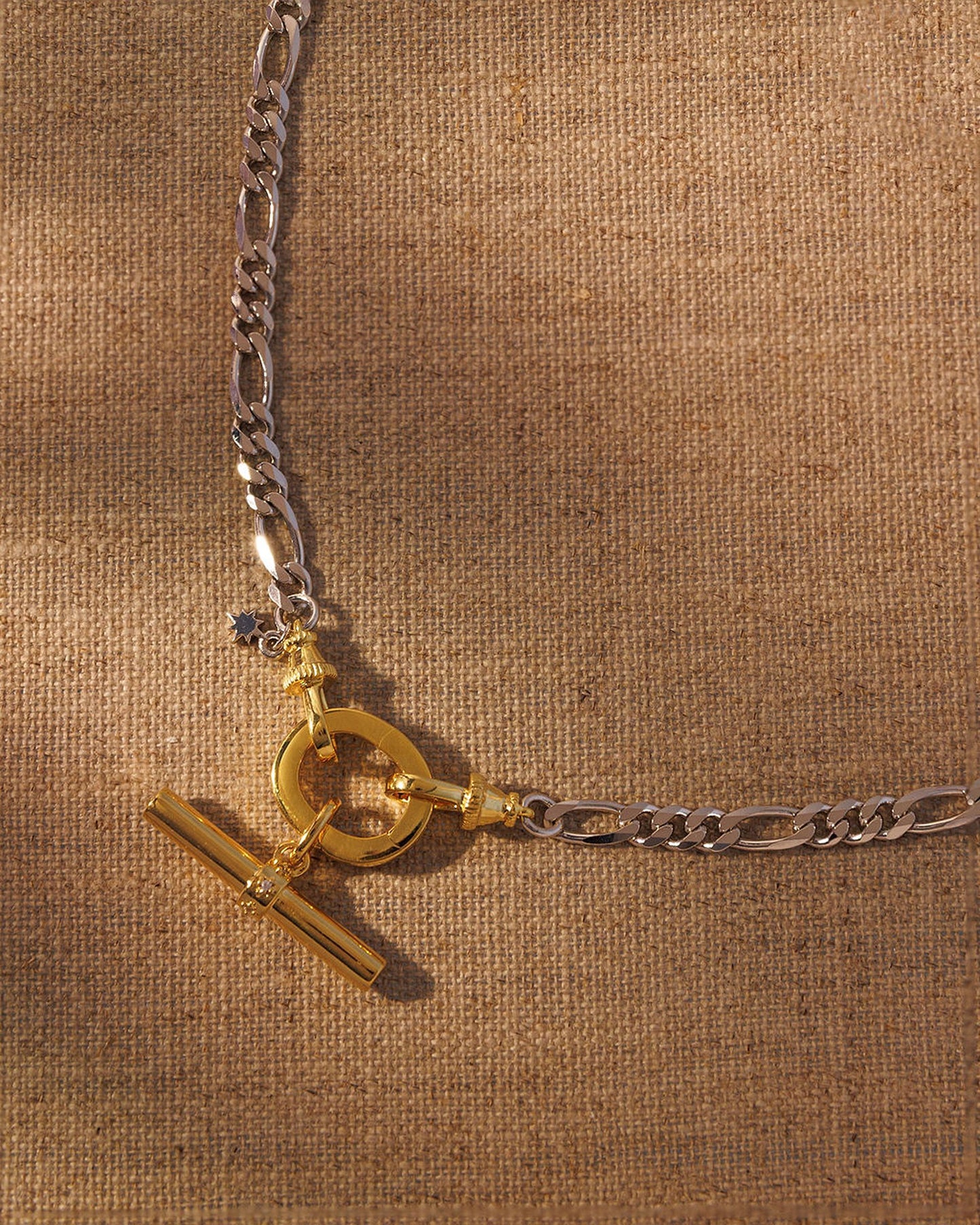 Mixed metal chain necklace with gold oval clasp and T-bar pendant charm attached to figaro chain