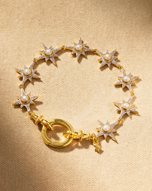 A gold-plated bracelet featuring a series of star-shaped connectors with cultured pearls, fastened with a lobster clasp on a textured background.