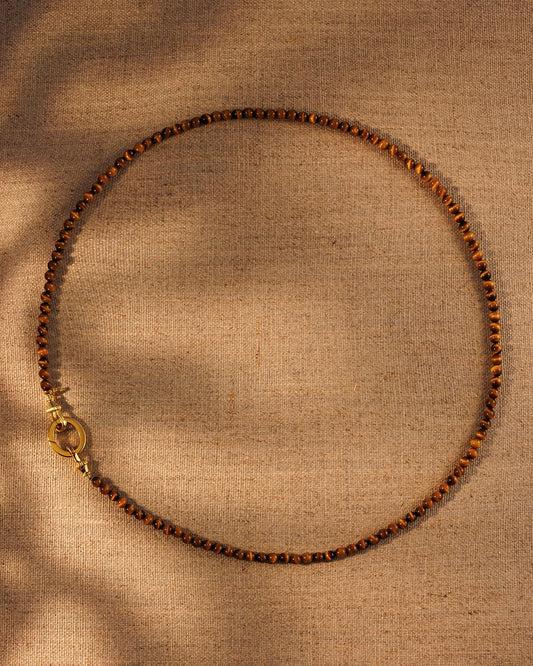 Tiger’s eye gemstone beaded necklace with gold oval clasp on textured background