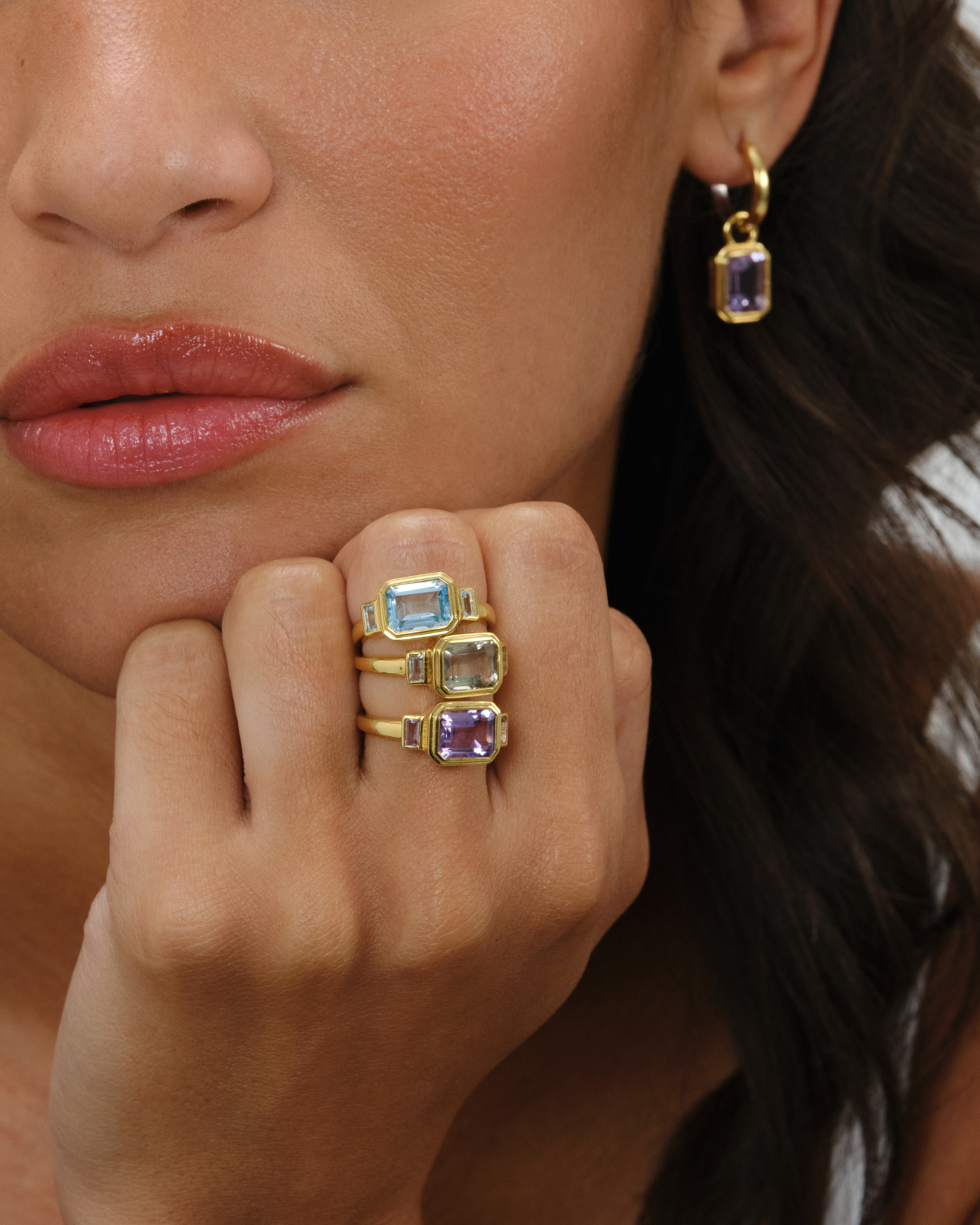Lumi emerald cut gemstone rings stacked in blue topaz, green emerald and pink amethyst with Cara hoop earring and amethyst charm in 18ct gold plated sterling silver