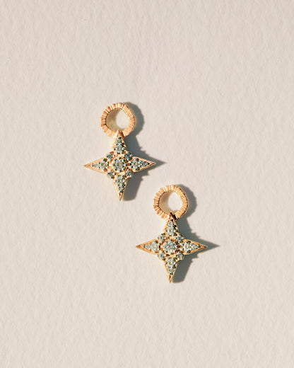 A pair of gold-plated earring charms with round brilliant cut white crystals, designed in a star shape, displayed against a neutral background.
